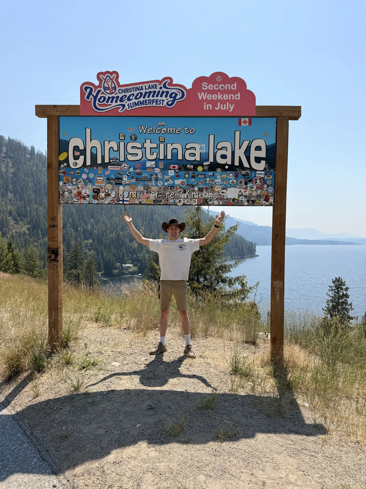 Arms out under the Welcome to Christina Lake sign