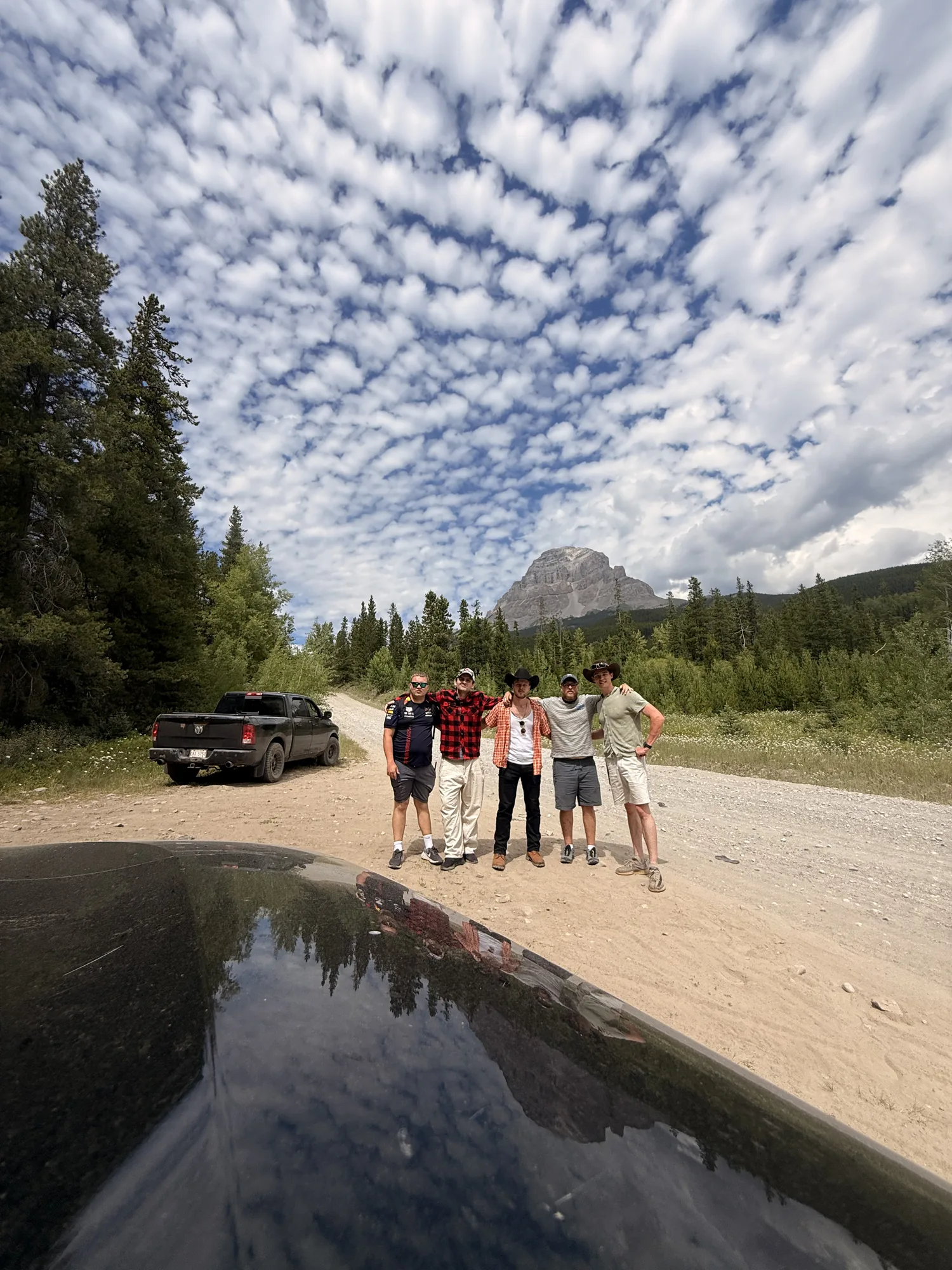 The truck and the group reflected in a puddle on a gravel road at Crowsnest Pass