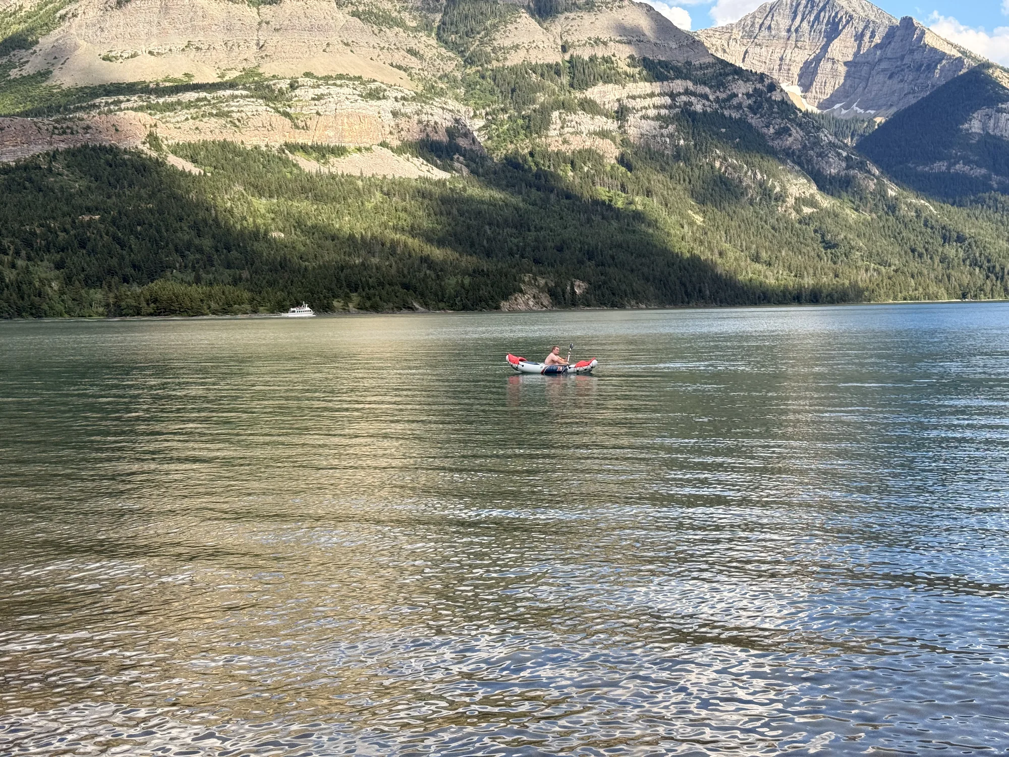 Kayakers on Upper Waterton Lake below a steep mountain wall