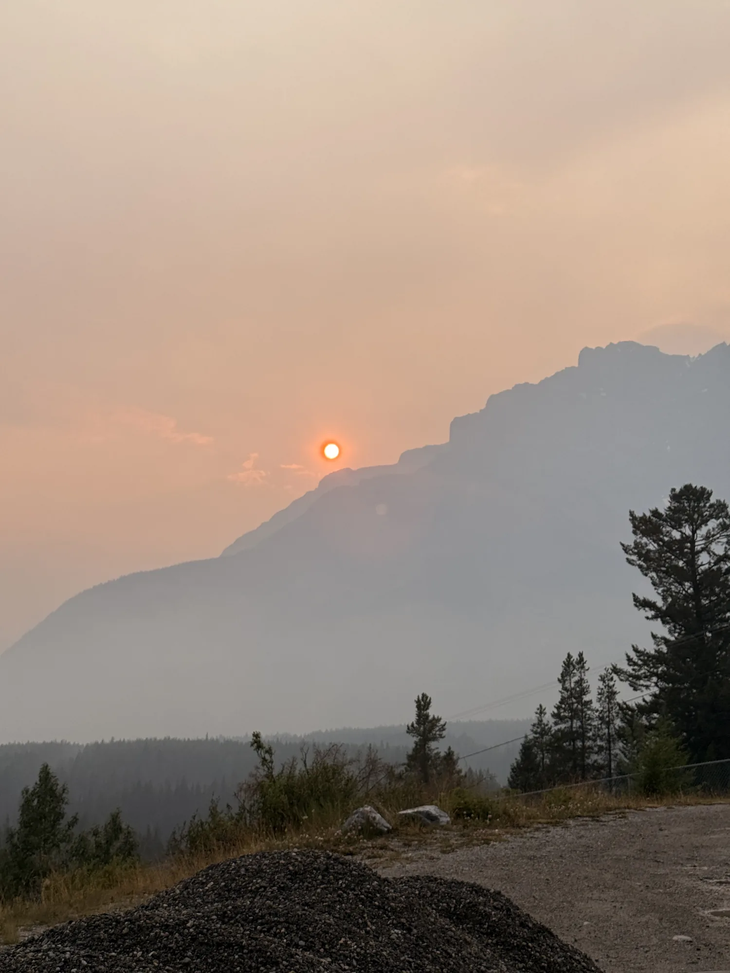 A red sun sinking through heavy wildfire smoke over the Banff mountains